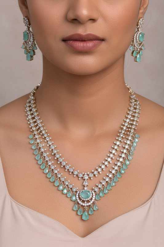 A three-layered gold-toned statement necklace with light blue-green stone accents and a matching pair of drop earrings, displayed on a white jewelry bust.