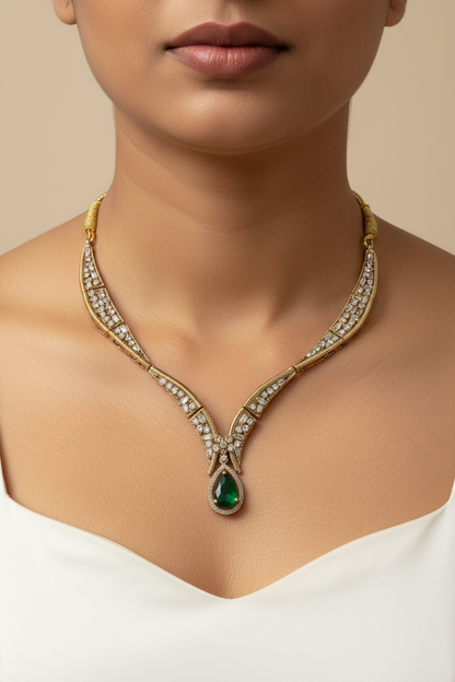 Gold jewelry set featuring a necklace, matching earrings, and a ring displayed on a white fabric jewelry bust. The pieces are decorated with clear stones and feature green gemstone accents.