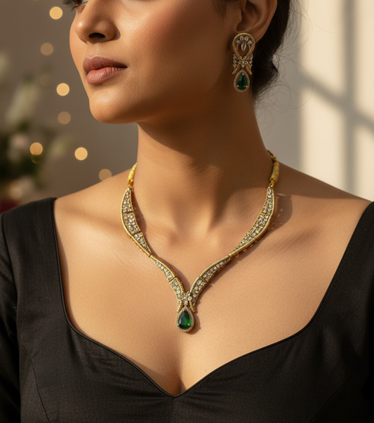 Gold jewelry set featuring a necklace, matching earrings, and a ring displayed on a white fabric jewelry bust. The pieces are decorated with clear stones and feature green gemstone accents.