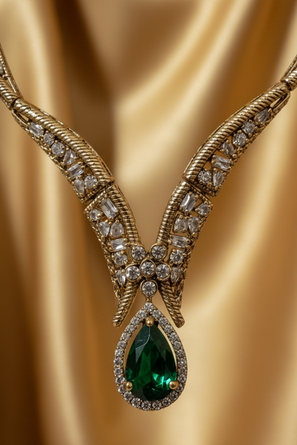 Gold jewelry set featuring a necklace, matching earrings, and a ring displayed on a white fabric jewelry bust. The pieces are decorated with clear stones and feature green gemstone accents.