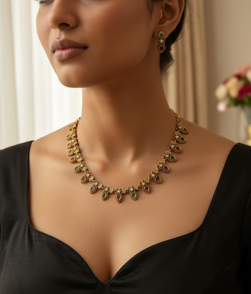 Gold-tone jewelry set featuring a necklace and matching earrings with small red and green teardrop-shaped stones, displayed on a white fabric jewelry bust.