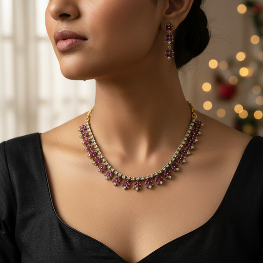 Gold-plated jewelry set featuring a necklace and matching drop earrings with deep purple gemstone floral motifs, displayed on a textured white jewelry bust.