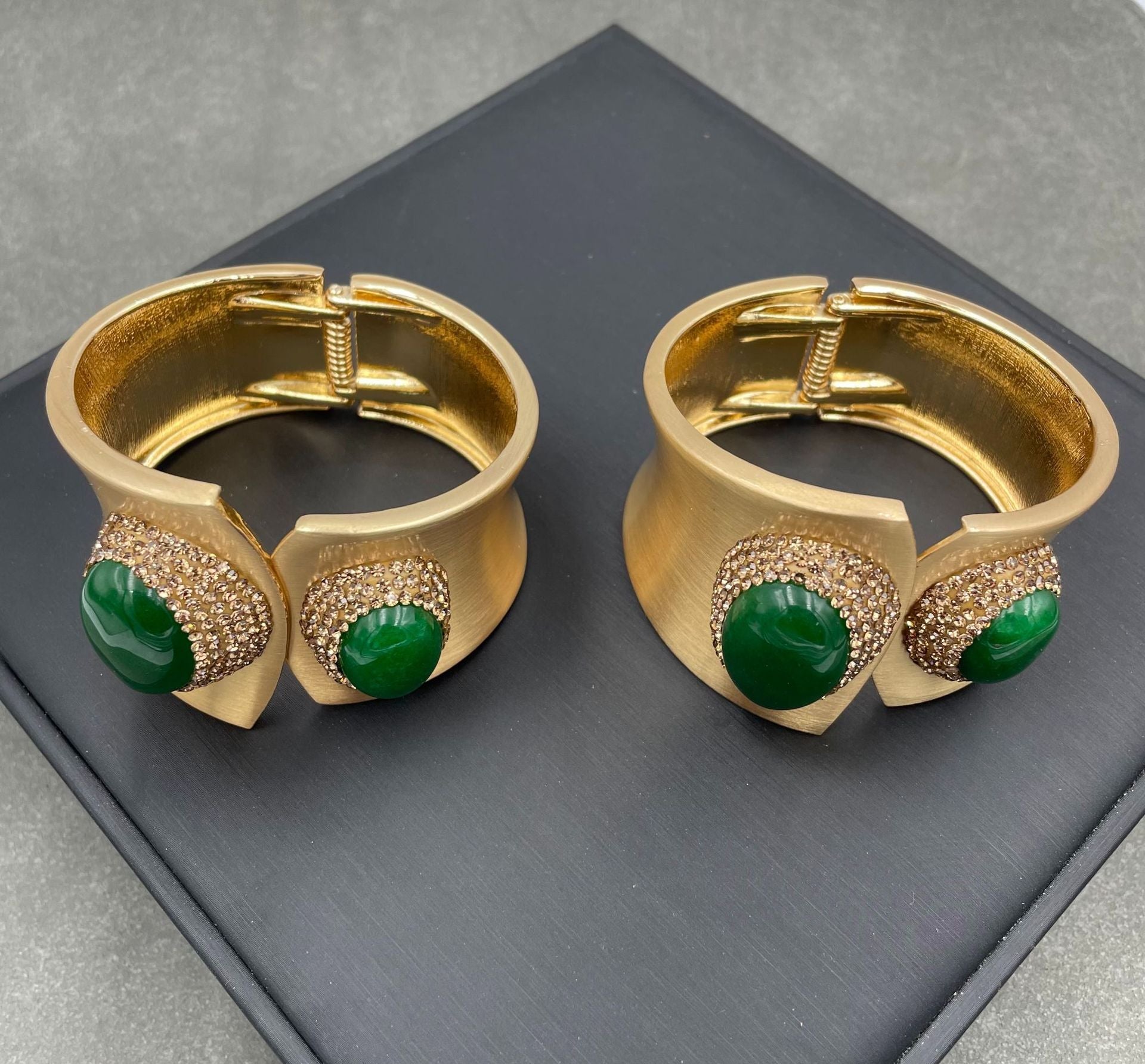 Pair of gold earrings with green gemstones on a dark surface