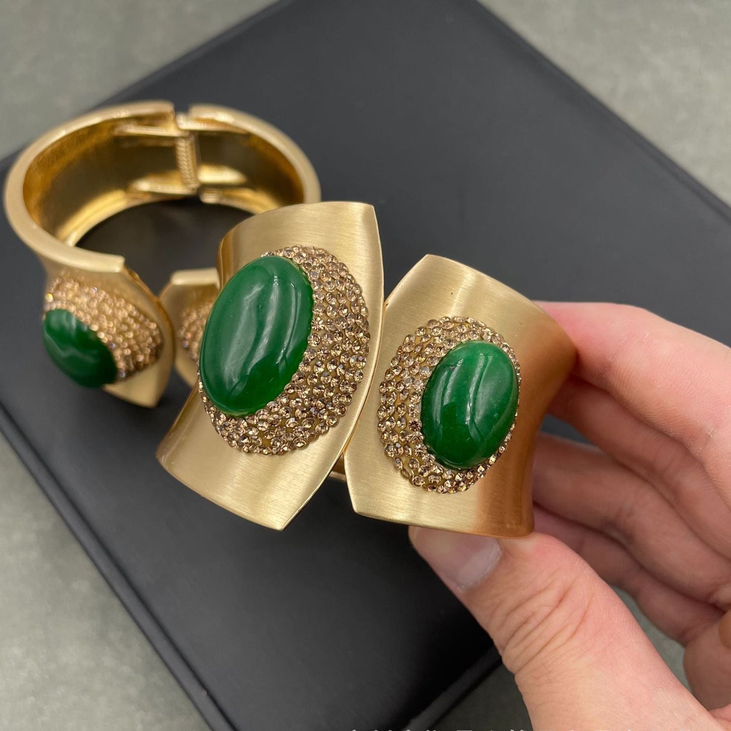 Gold bracelet with green stones held by a hand on a dark surface