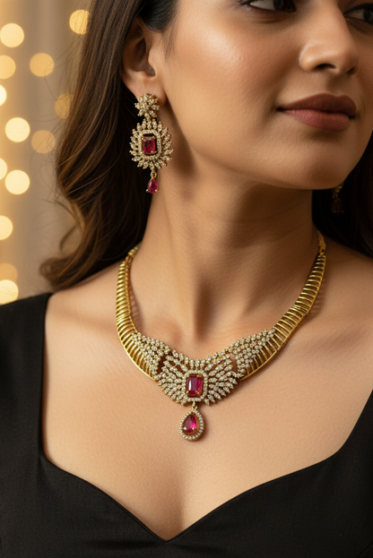 Gold-toned traditional necklace set with a matching maang tikka, displayed on a white jewelry bust. The necklace features intricate gold filigree, clear stones, and red gemstone accents, with a matching pendant on the bust.