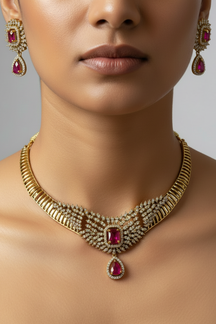 Gold-toned traditional necklace set with a matching maang tikka, displayed on a white jewelry bust. The necklace features intricate gold filigree, clear stones, and red gemstone accents, with a matching pendant on the bust.