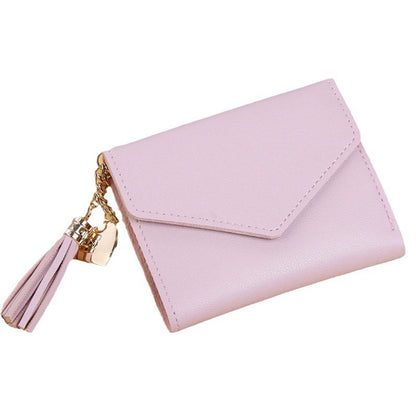 A light pink faux leather wallet with an envelope-style flap and a gold-tone tassel charm, shown on a plain white background.